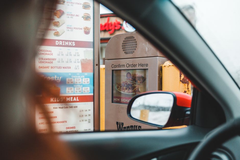 Blurred driver choosing food from menu and telling order to drive thru speaker post