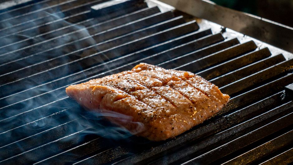 Close-up of a juicy salmon fillet sizzling on an outdoor grill, surrounded by aromatic smoke.