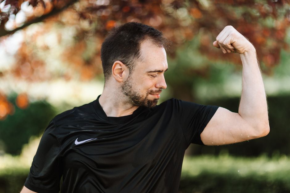 A man flexing his bicep outdoors, wearing a black shirt. Fitness and strength concept.