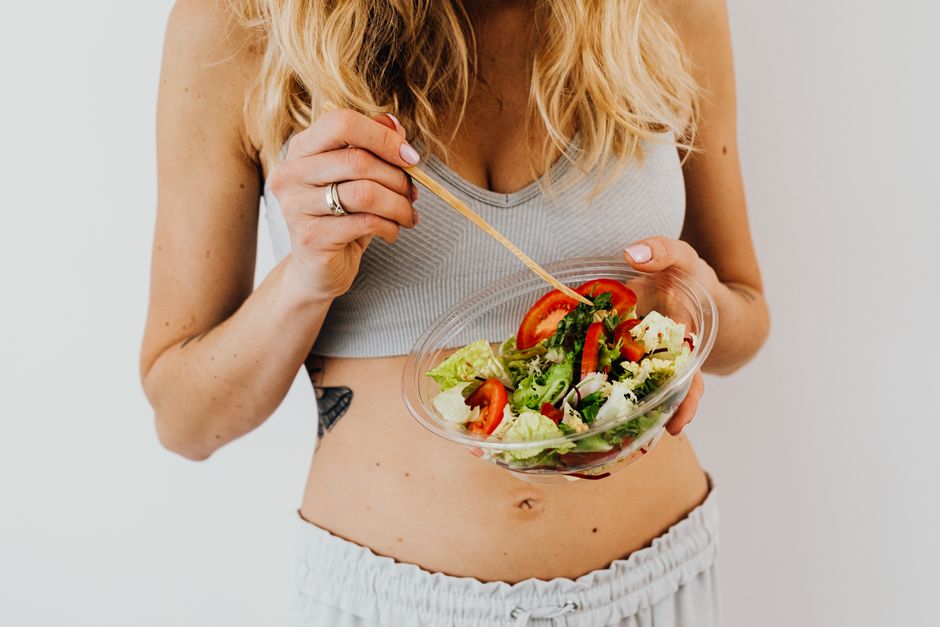 Woman in sports attire enjoys a fresh, nutritious salad, embodying a healthy lifestyle.
