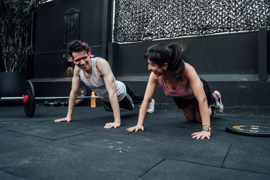 Man and woman doing pushups while smiling during a workout inside a Mexico City gym.