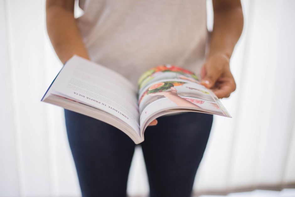 Close-up of a woman holding an open cookbook with colorful food images.